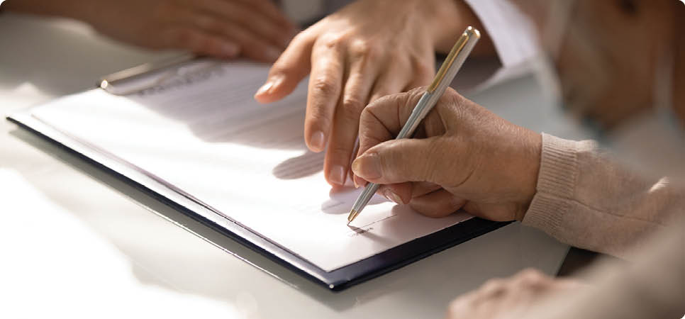 Commercial medicine. Close up of aged woman patient hand signing medical insurance contract at doctor office. Female medic show retired lady client place to put signature on healthcare coverage policy